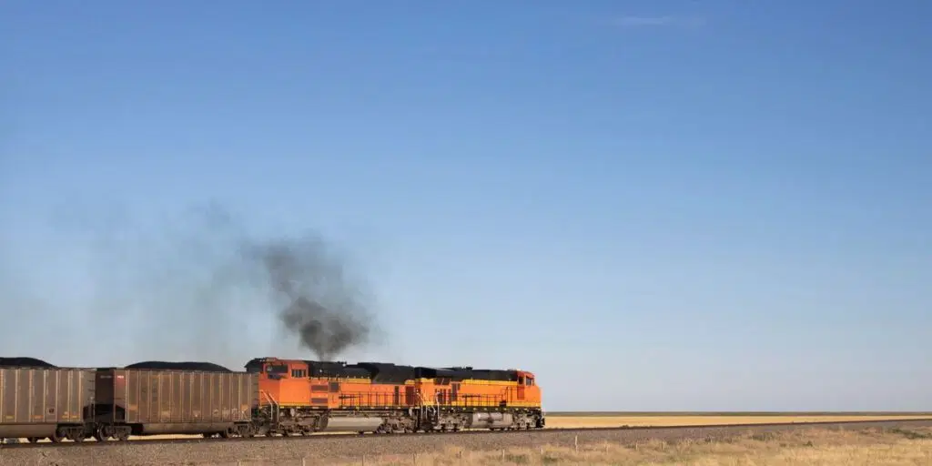 The front part of train composition with orange locomotive with dark smog cloud from diesel engine in Kansas prairie